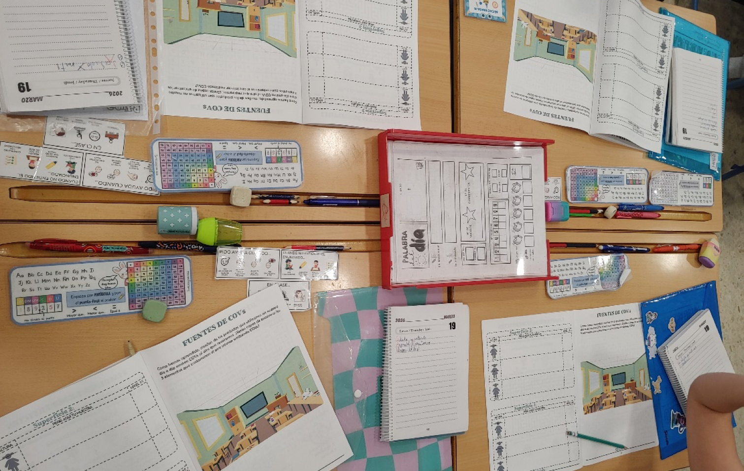 Overhead view of classroom desks with EDIAQI IAQ worksheets titled “Fuentes de CO₂”, alongside pencil cases, rulers, erasers and notebooks arranged around pupils’ workspaces.