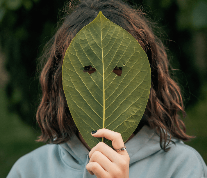A person covering their face with a leaf